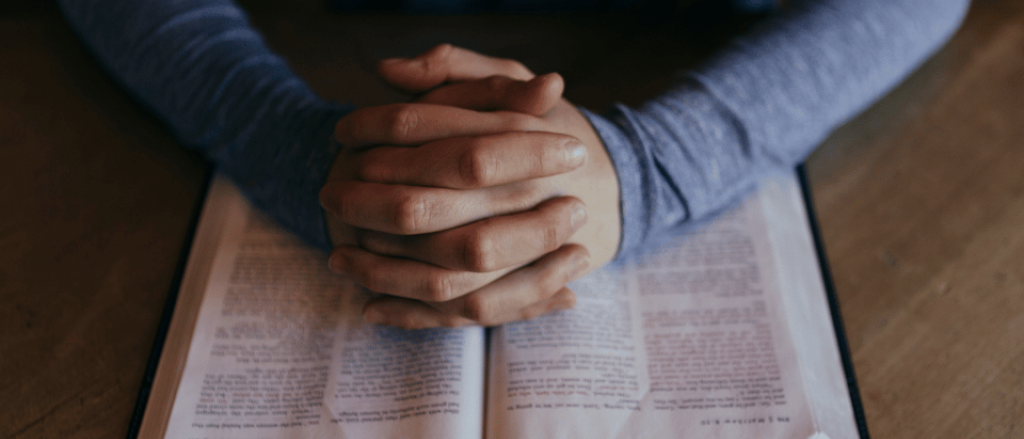 Hands folded prayerfully on Bible